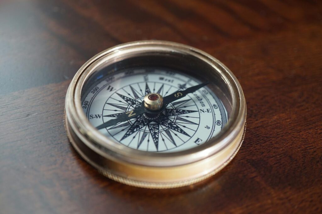 Close-up of a vintage compass resting on a warm, dark wooden surface, indicating navigation and exploration.
