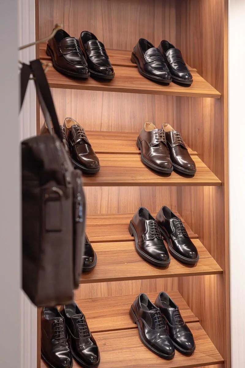 Collection of polished men's dress shoes displayed on wooden shelves in an organized closet.