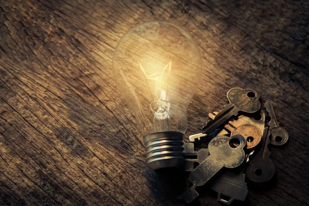 Illuminated vintage light bulb beside keys on rustic wooden table, symbolic of ideas.