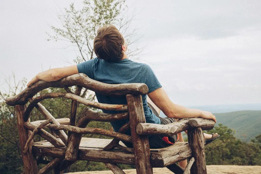 A man enjoys a tranquil moment on a wooden bench overlooking a scenic mountain landscape in New York.