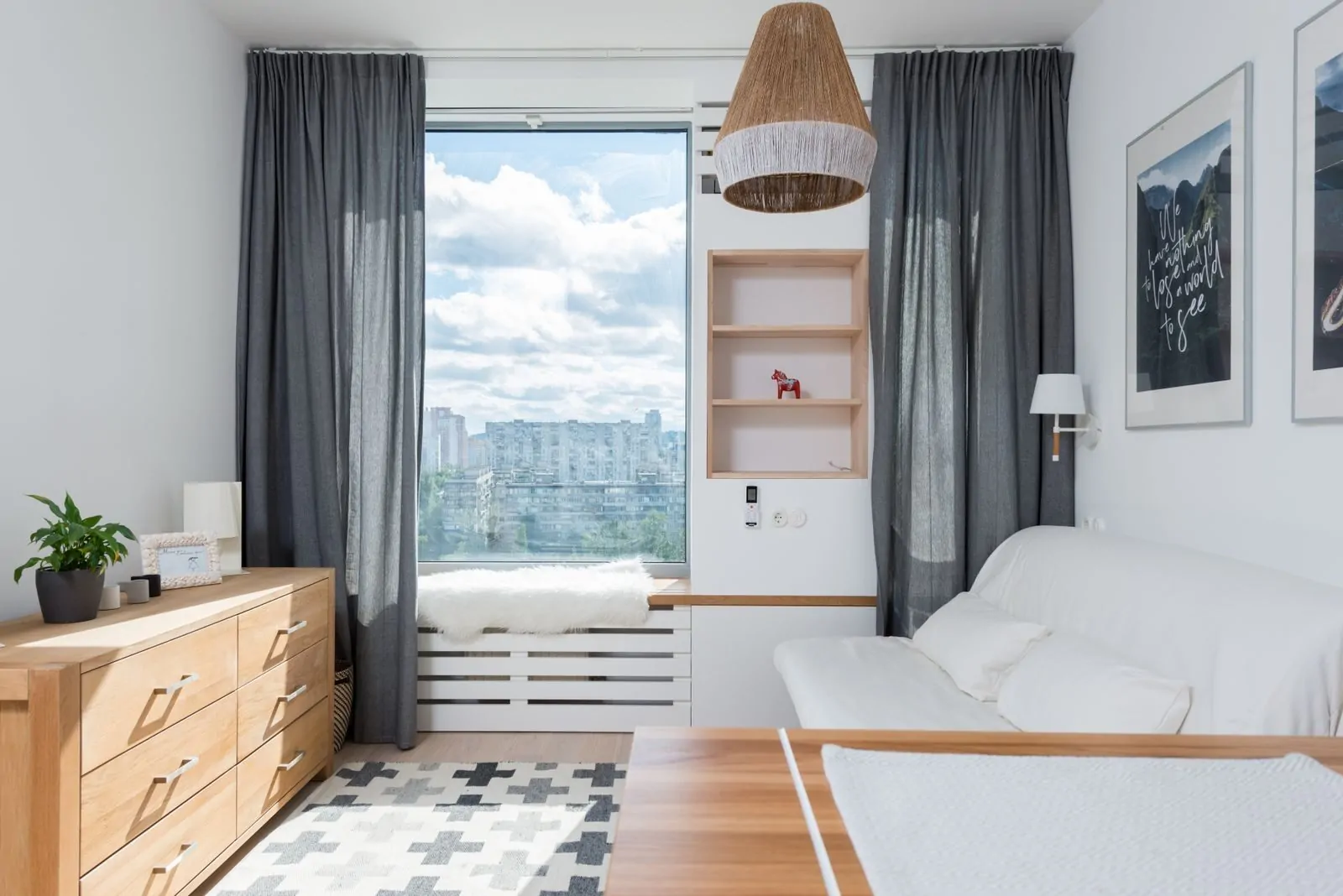 35+ Room Decor Ideas for Small Spaces That Feel Bigger 26 Wooden table and drawer near white couch at wall decorated with paintings and shelves with decorations in stylish room with sunlight