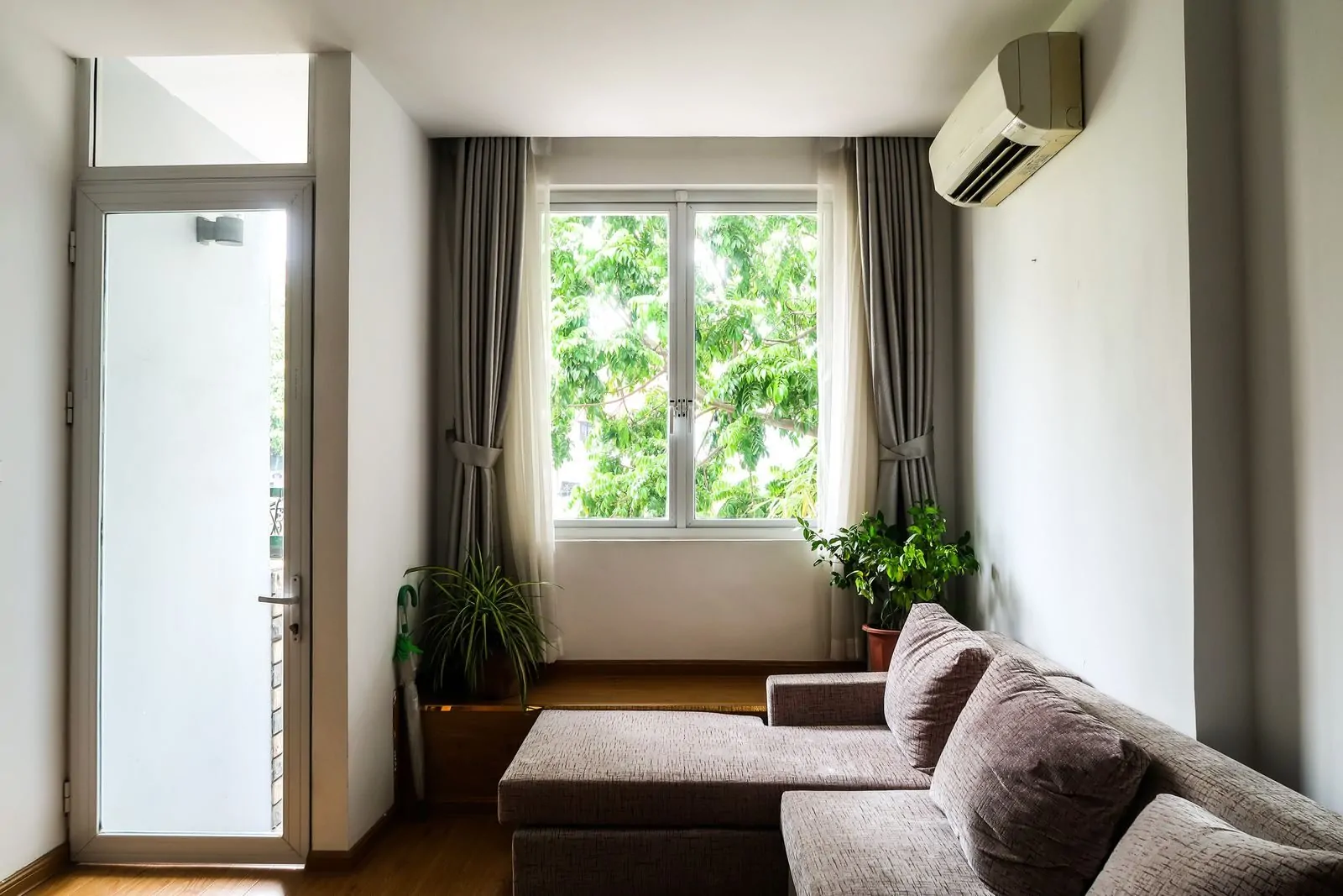35+ Room Decor Ideas for Small Spaces That Feel Bigger 24 Bright living room with a cozy sofa, indoor plants, and a large window with curtains.