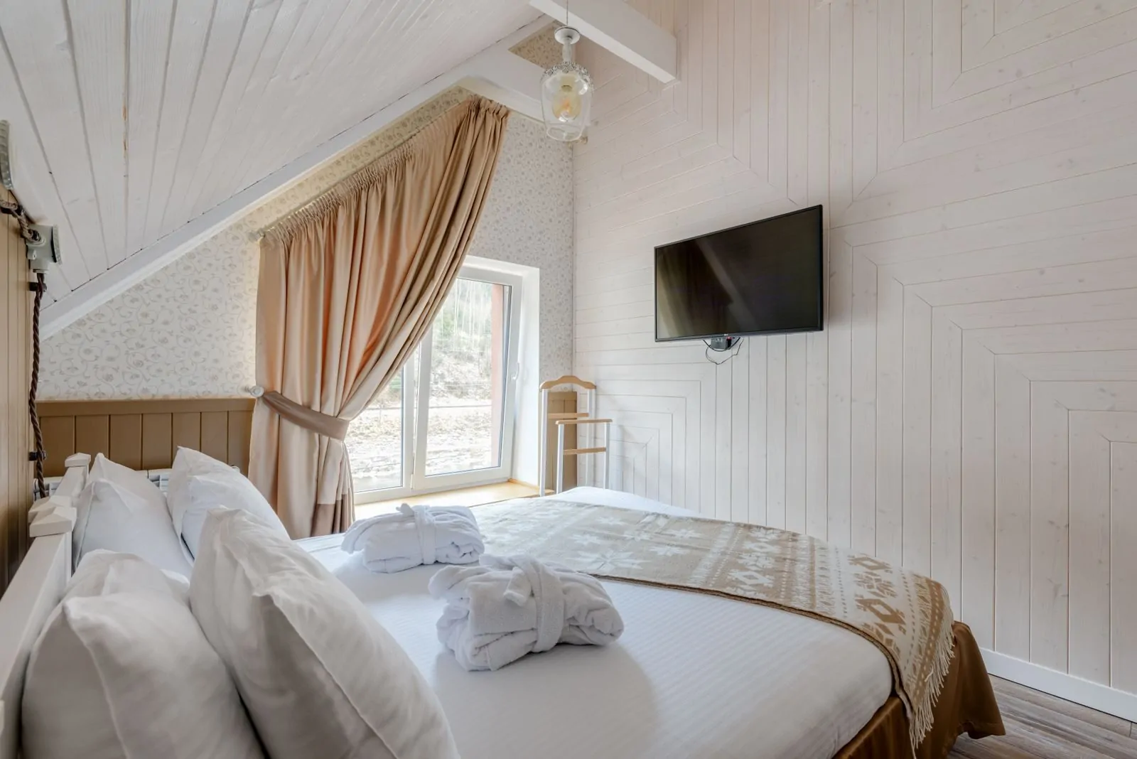35+ Room Decor Ideas for Small Spaces That Feel Bigger 34 Cozy attic bedroom featuring modern decor with a wall-mounted TV and elegant linens.