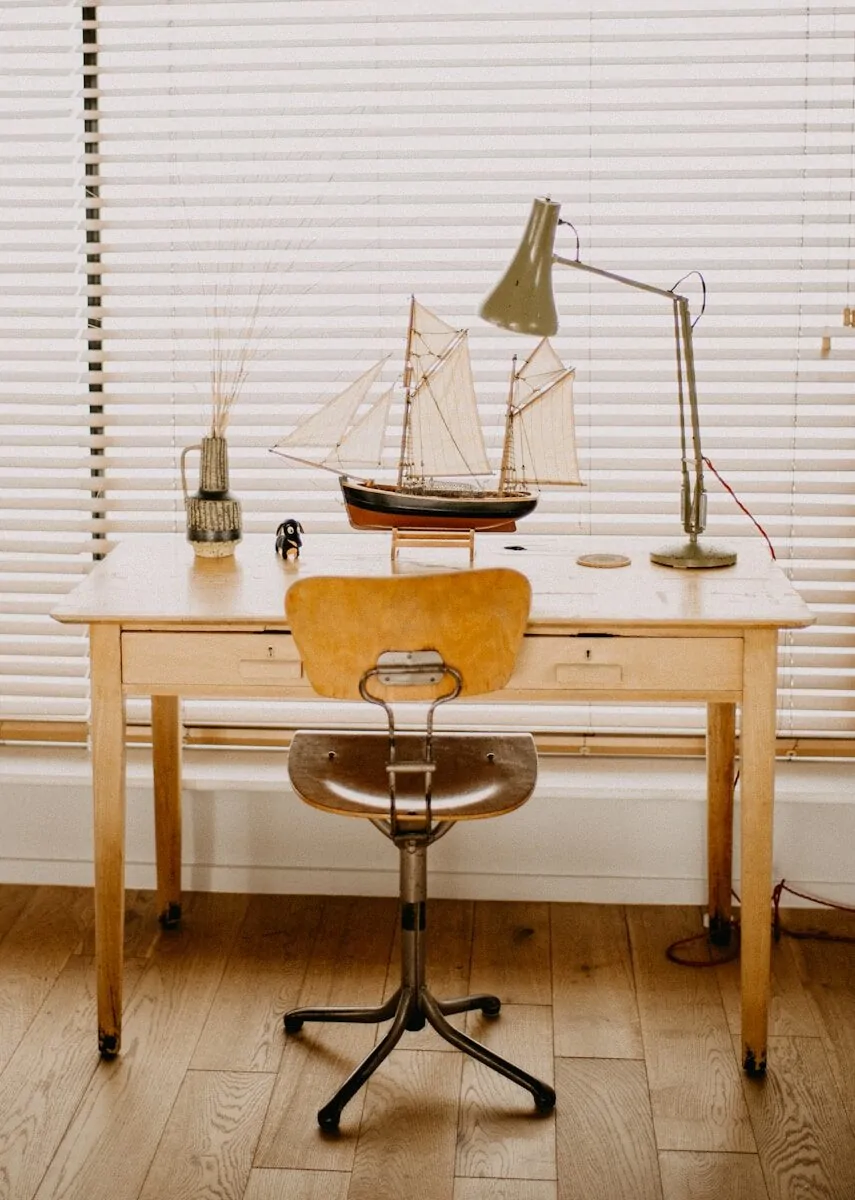 35+ Small Office Ideas for Working From Home 11 Desk with model ship and lamp in front of blinds.