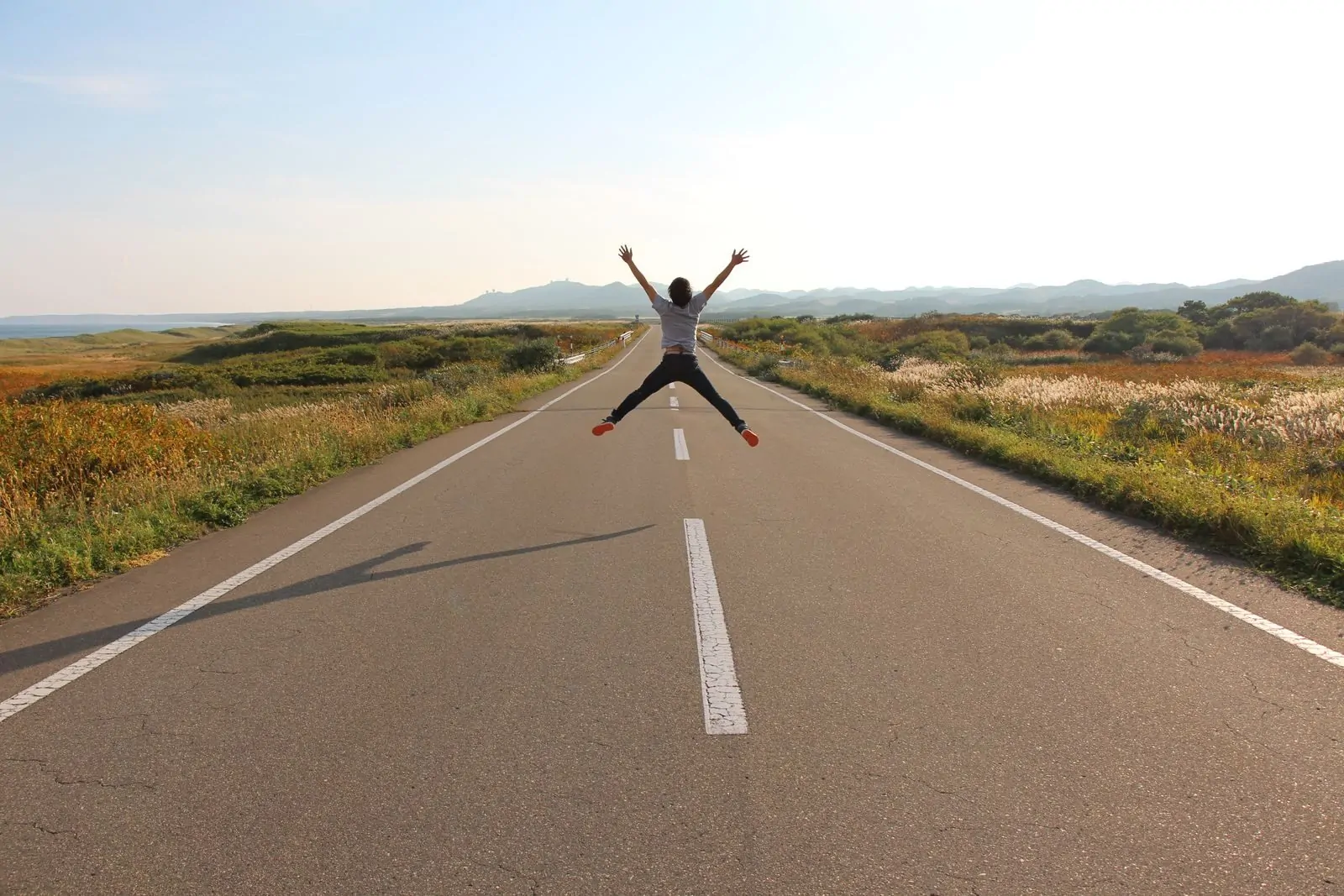 Person jumping on an open road in Hokkaido's scenic landscape on a sunny day.