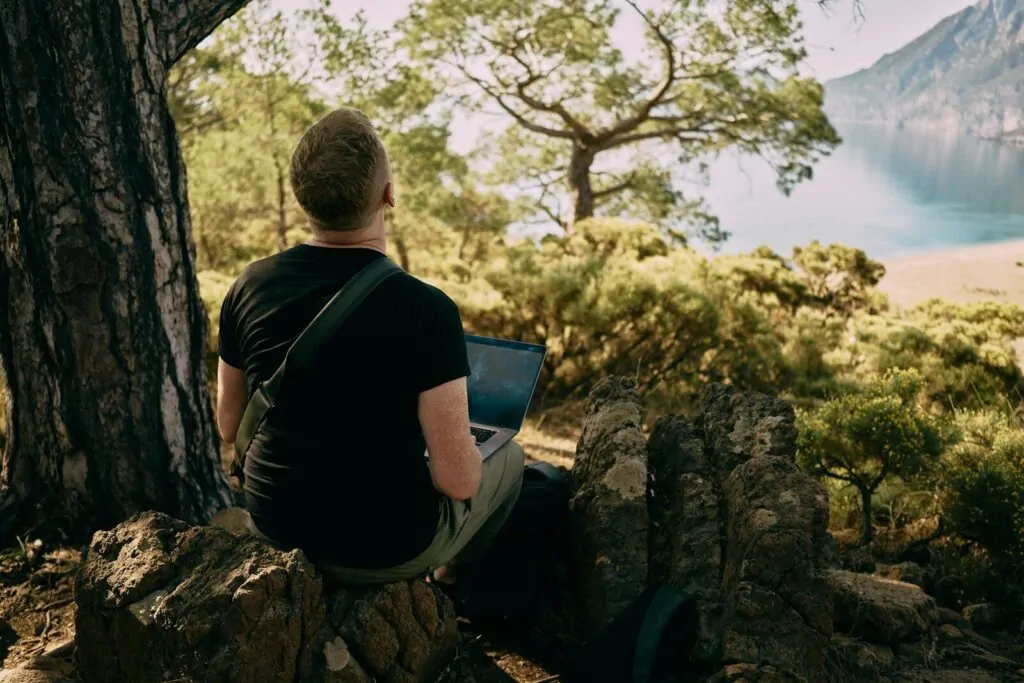 4 High-Paying Remote Jobs That Pay $100K Without a Degree 1 a man sitting on a rock with a laptop in his lap