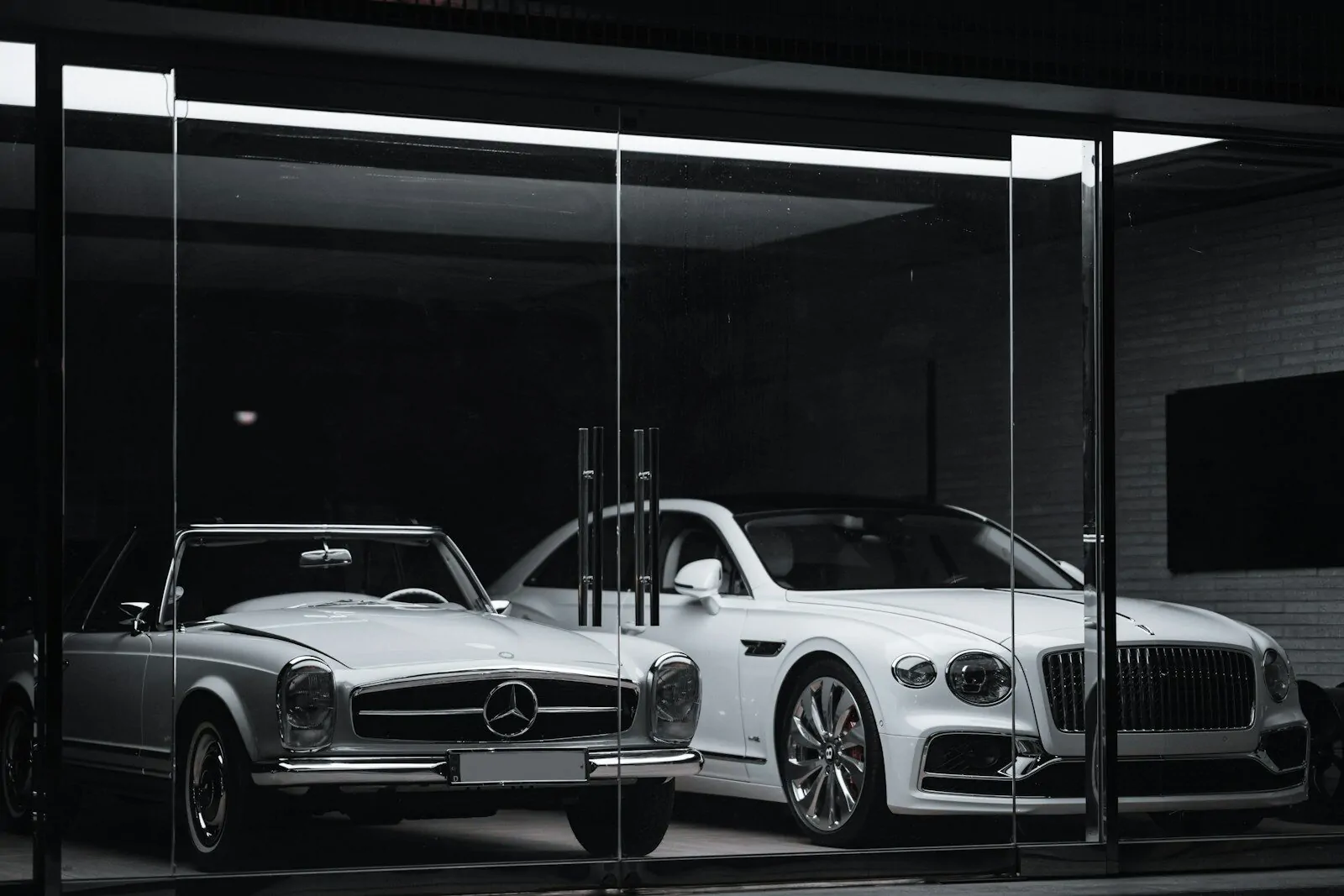 A vintage Mercedes-Benz and a modern Bentley parked behind a glass storefront