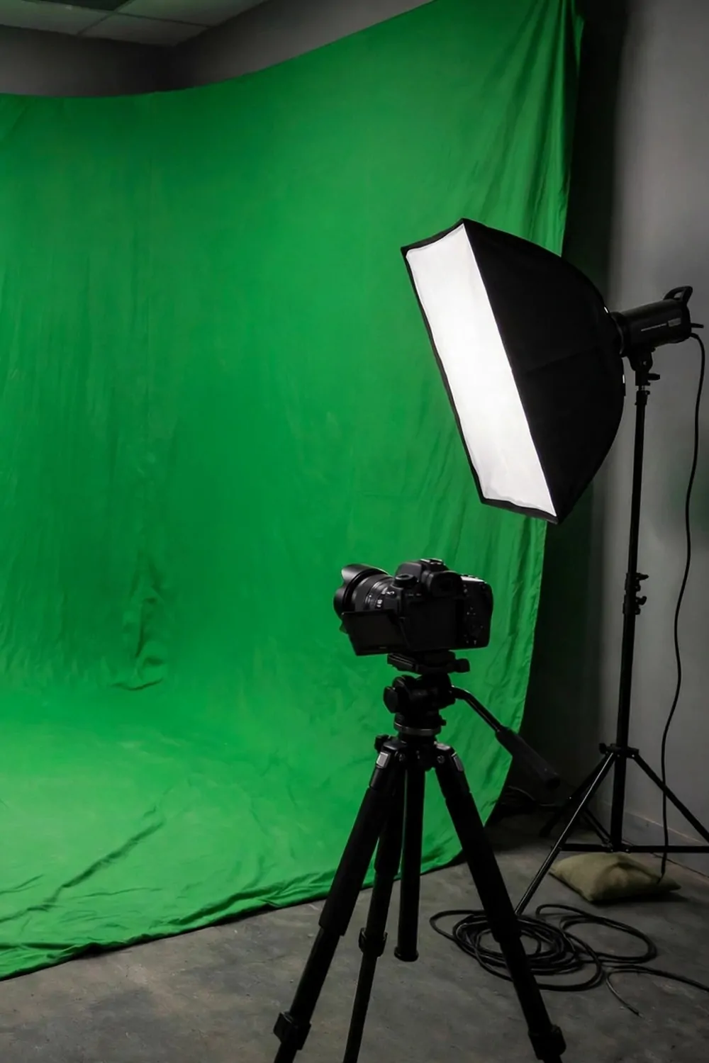 A green screen cove studio corner with a curved green backdrop, one softbox light and a camera on a tripod