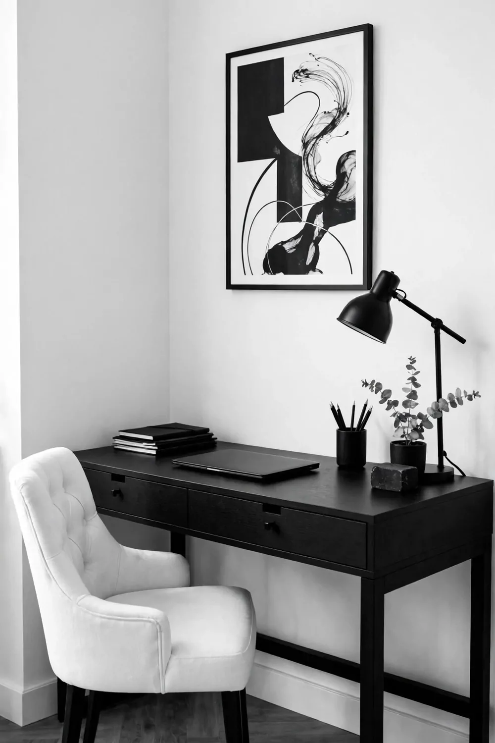20 Office Inspiration Workspaces That Look Straight Out of a Magazine 14 A black desk, white tufted chair, black lamp, closed blank laptop, and wordless black-and-white abstract art in a thin black frame against white walls.