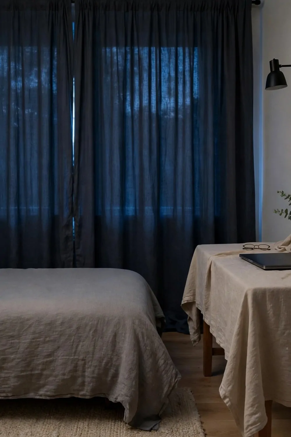 A tidy bedroom office at night, laptop closed, lamp off, desk covered with a cloth, bed made, curtain drawn, calm evening light