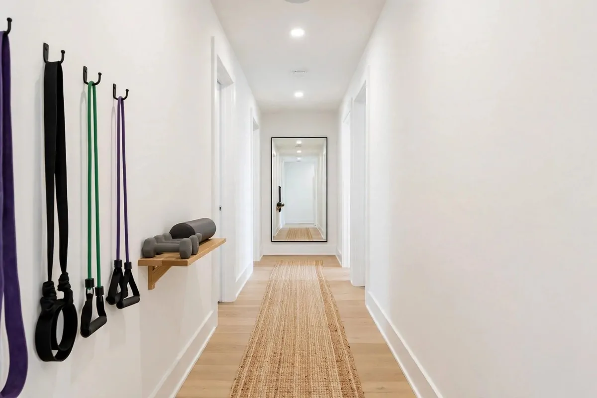 21 Small Workout Space at Home Setups That Actually Work 17 A long narrow hallway with a slim runner mat, resistance bands on wall hooks, a small shelf with dumbbells and a mirror at one end