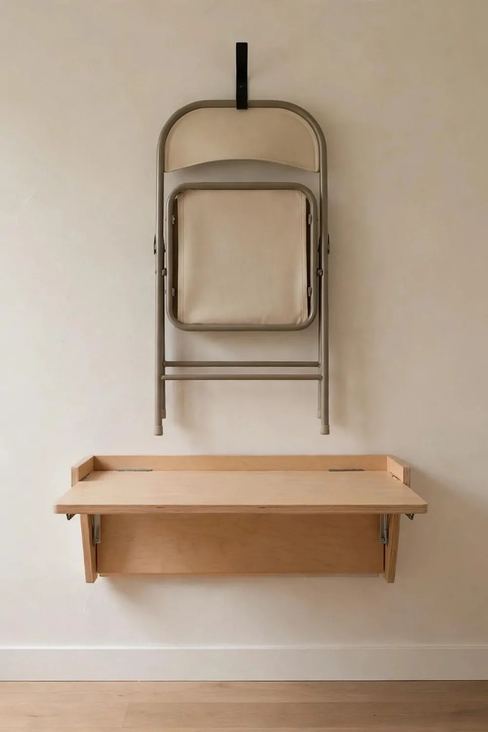A folding chair hanging flat on a wall hook in a small home office, desk folded down below it, tidy empty floor