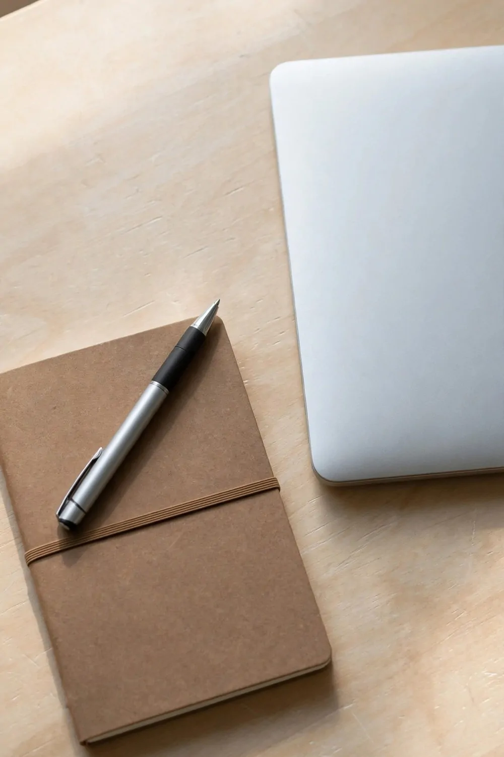 One pen and one notebook on a clear desk, laptop closed beside them