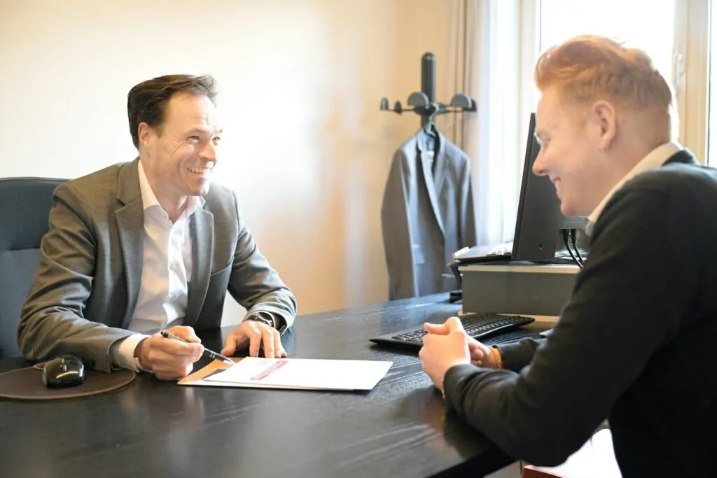 Two smiling men discussing documents at an office desk
