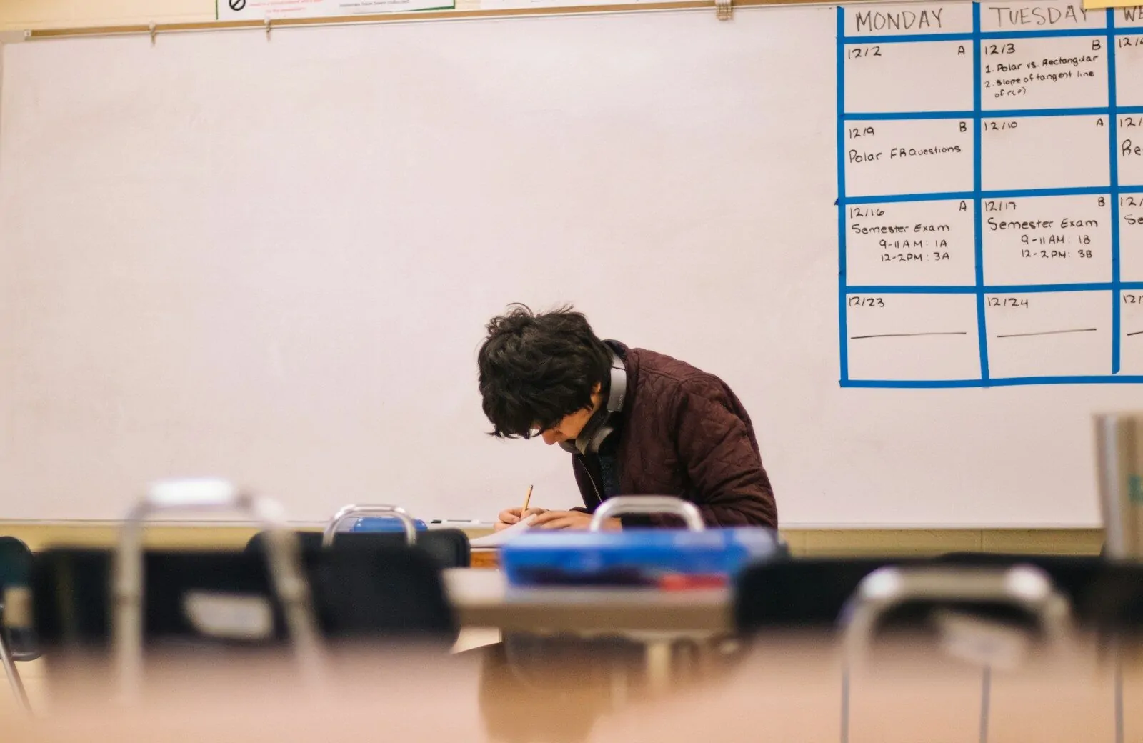 A student writing on paper at a desk in a classroom