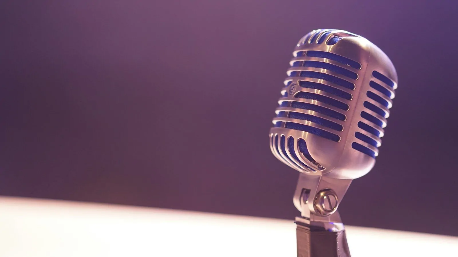 A vintage silver microphone with blue accents against a soft purple background